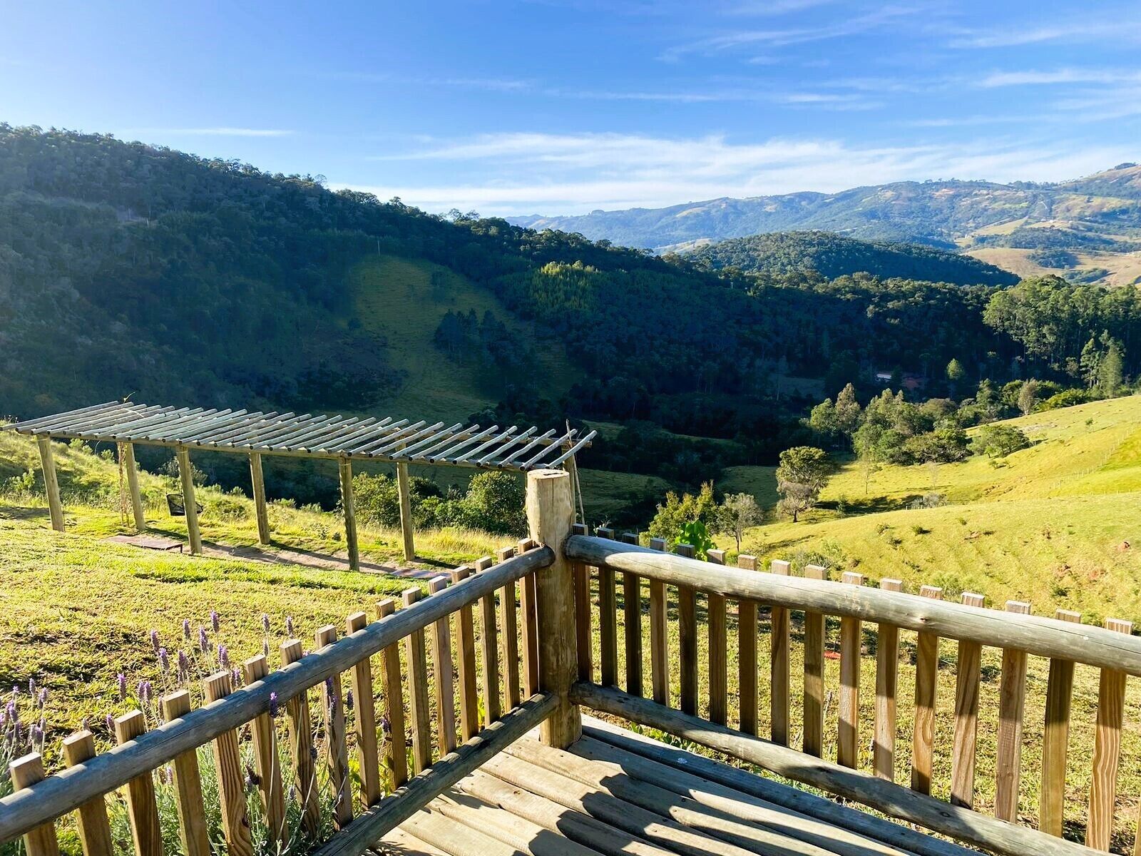 Una terraza de madera con barandilla que da a un valle con colinas y árboles.