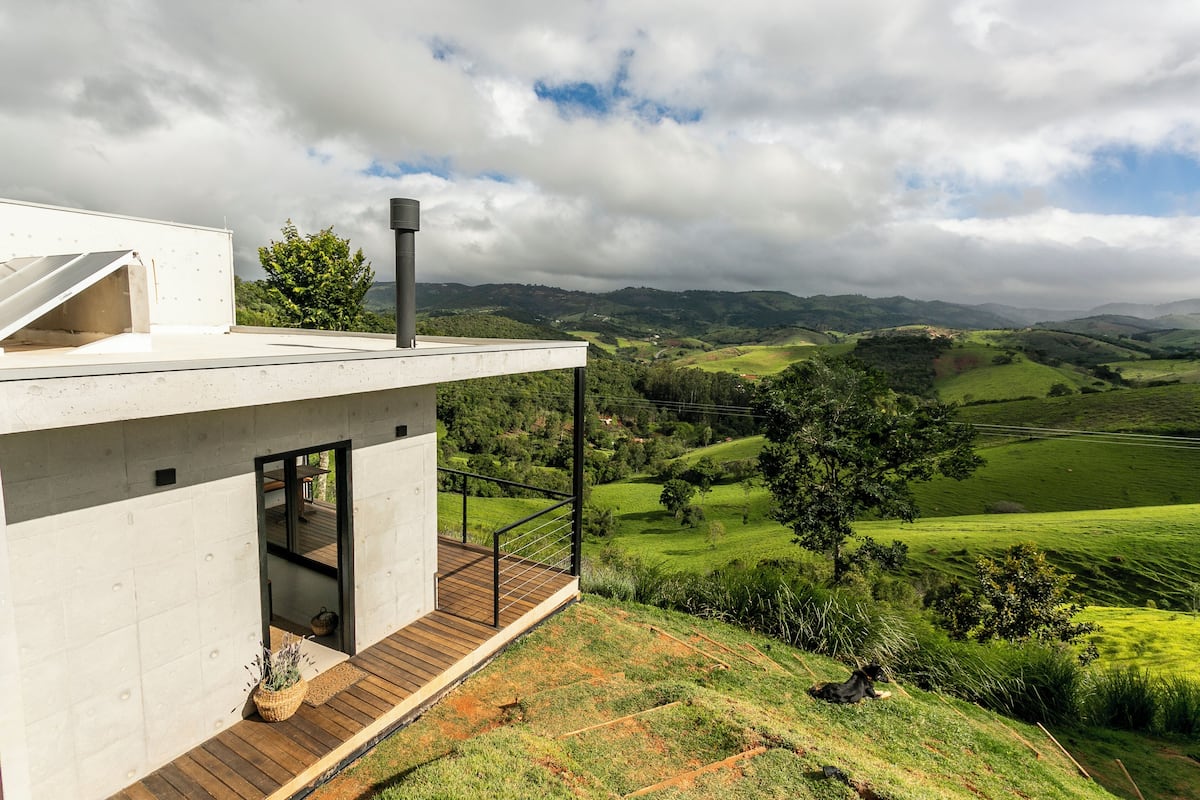 A modern house with a wooden deck and a large window overlooking a green valley.