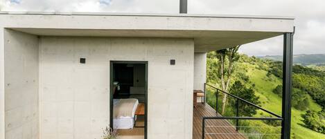 A modern, minimalist bedroom with a wooden deck and a view of a lush valley.
