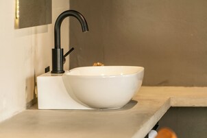 Un baño moderno con un lavamanos blanco, un grifo negro y un espejo rectangular encima.
