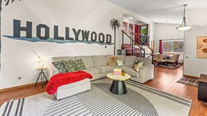 Un salon agrémenté d’une grande fresque murale sur le thème d’Hollywood, avec un canapé, une table basse et un escalier menant à une salle à manger.