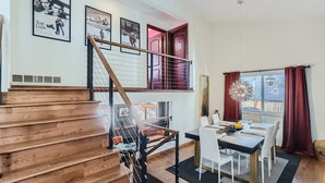 Un intérieur moderne avec un escalier en bois, un coin repas doté d’une table noire et des affiches encadrées accrochées au mur.