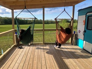 Una terraza de madera con dos hamacas colgadas del techo, con vistas a un campo cubierto de hierba.