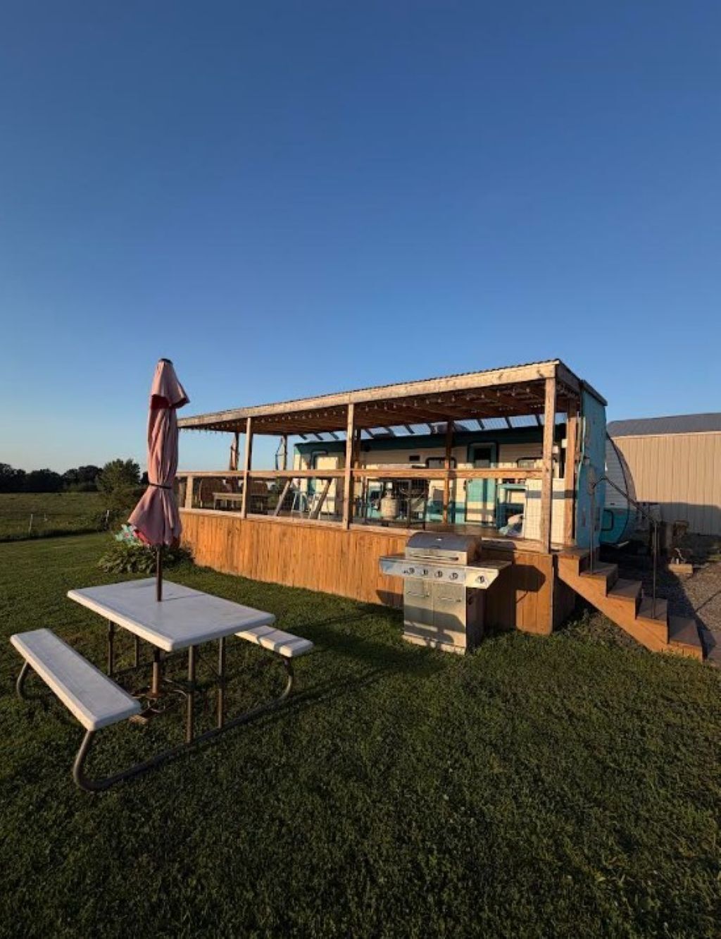 A wooden structure with a covered patio area, a grill, and a table with benches.
