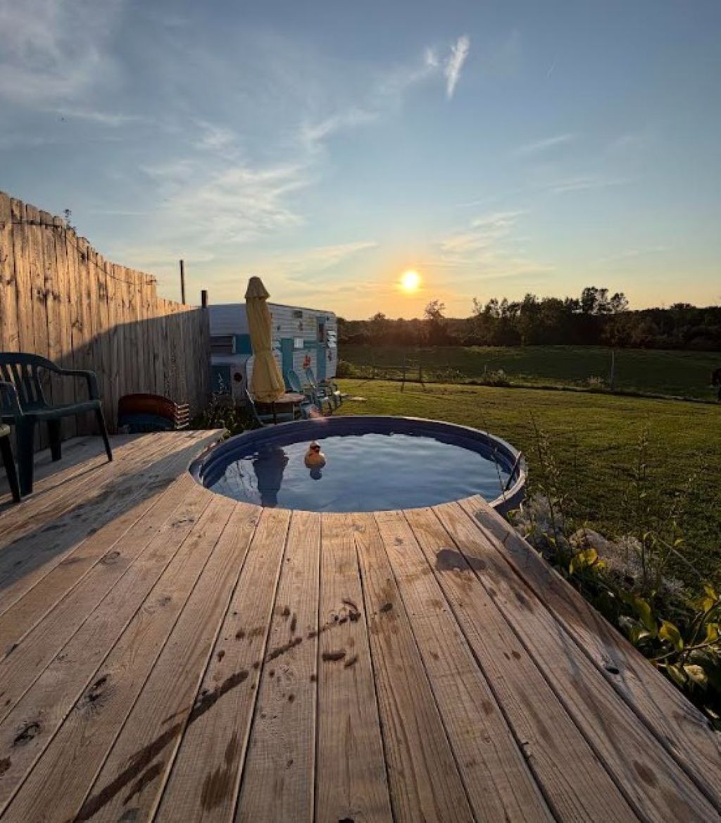 A wooden deck with a hot tub, a wooden fence, and a clear sky with the sun setting.