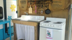 Cocina compacta con lavabo, estufa y utensilios colgantes.