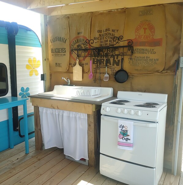 A compact kitchen with a sink, stove, and hanging utensils. - Relax and unwind at The Happy Camper Scottsville! (Scottsville)