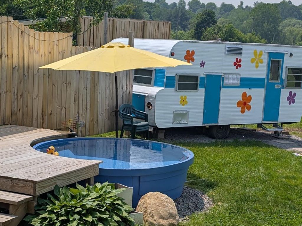 Un patio trasero con piscina, terraza de madera y una caravana recreativa colorida.