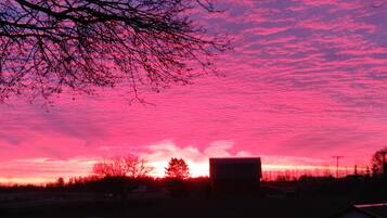 A sunset over a rural landscape with a barn and open fields.