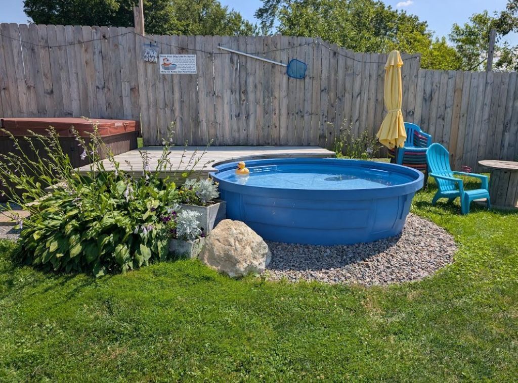 Un patio trasero con una piscina elevada azul, cerca de madera, un jacuzzi y mobiliario exterior.