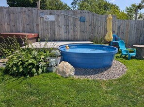 Un patio trasero con una piscina elevada azul, cerca de madera, un jacuzzi y mobiliario exterior.