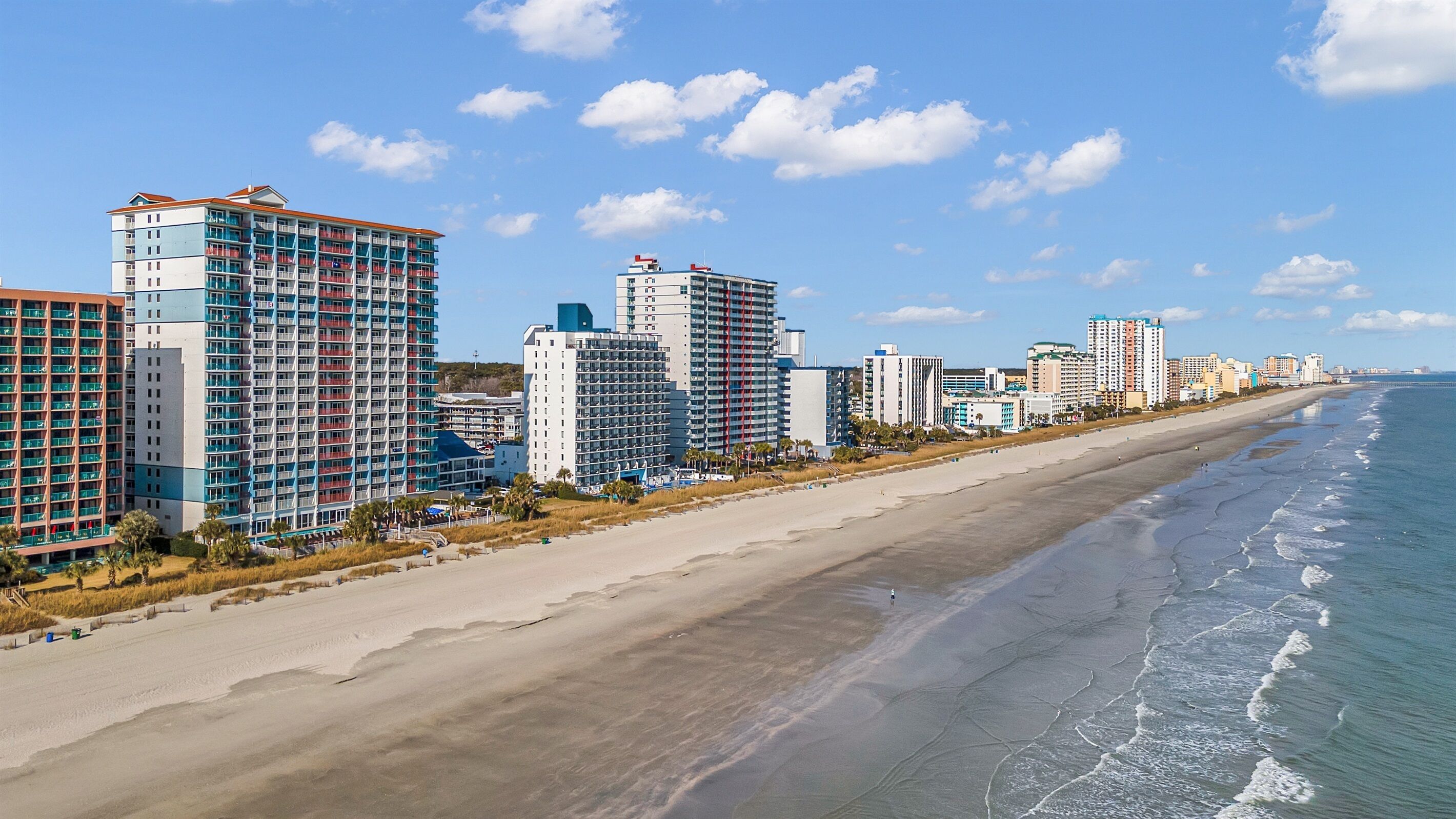 A coastal cityscape with high-rise buildings along the beach, featuring a sandy shoreline and ocean waves.