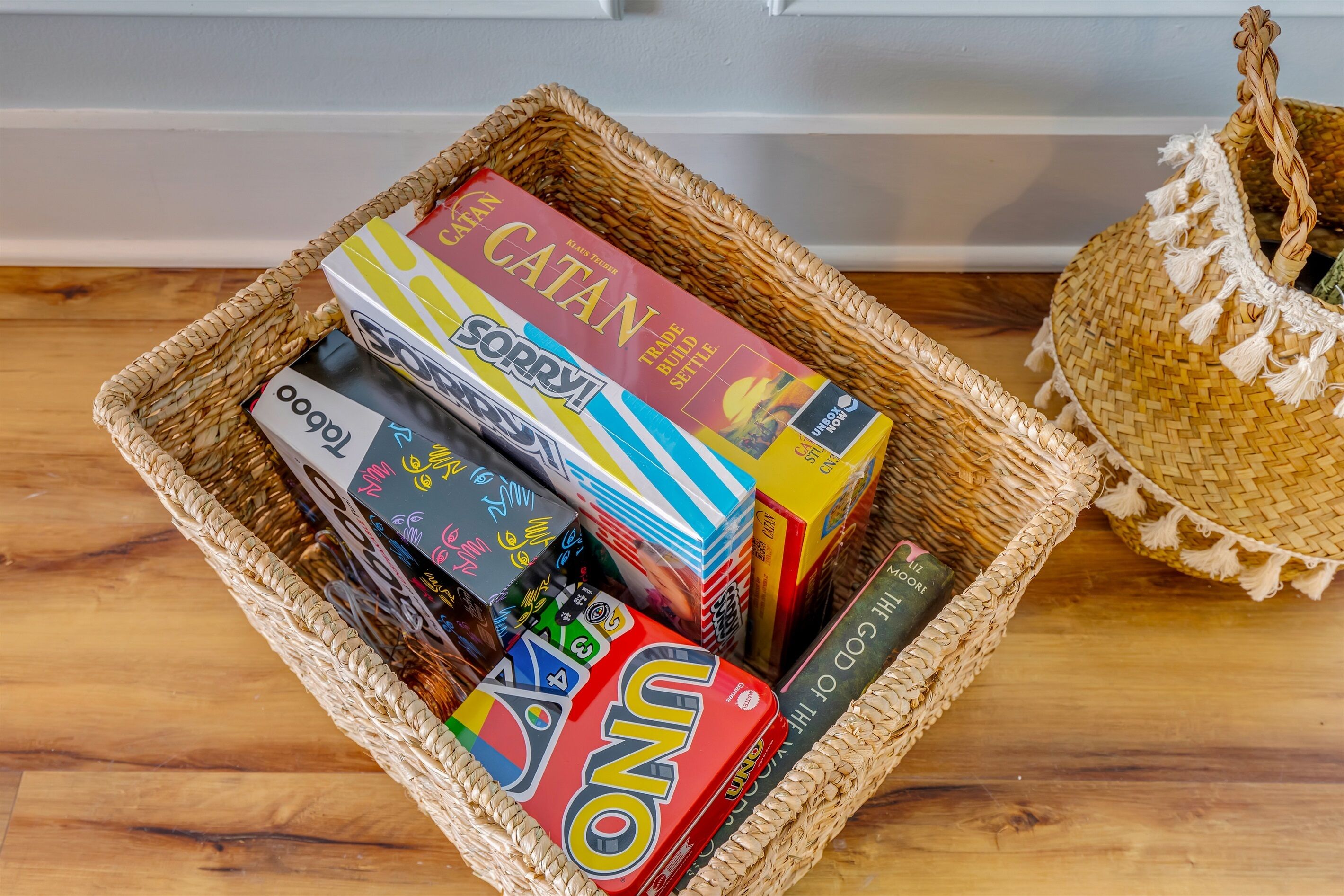 A wicker basket filled with board games and books on a wooden floor.