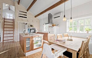 Una cocina con vigas de madera, una isla central y un comedor con mesa y sillas.