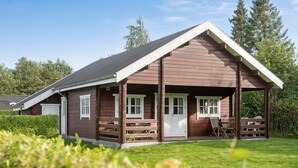 Eine Holzhütte mit Veranda, Fenstern mit weißen Rahmen und einem geneigten Dach.