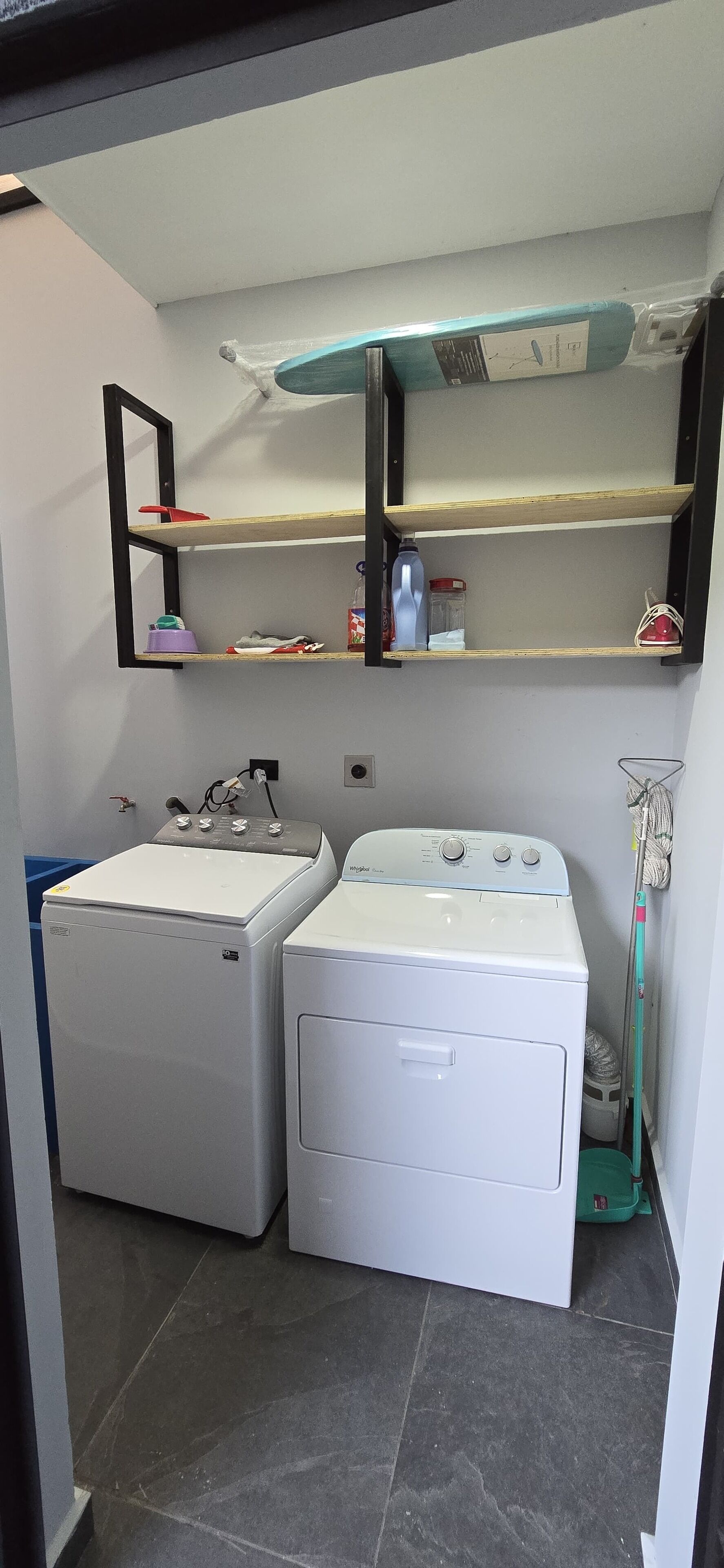 A compact laundry room with two white washing machines, a sink, and a mirror above the machines.