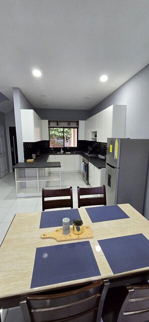 Eine moderne Küche mit weißen Schränken, einem Esstisch mit blauen Platzsets und einem Kühlschrank.