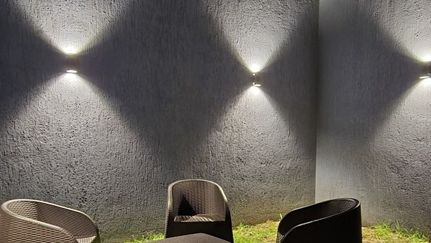 Un espacio de estar al aire libre con sillas de mimbre y un muro de hormigón con luces integradas.