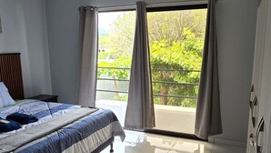 Habitación de hotel con cama, armario, ventana con cortinas y balcón con plantas.