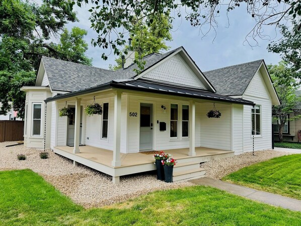 A single-story house with a covered porch, numbered 502, surrounded by a well-maintained lawn and gravel driveway. - Historic Home in Old Town Loveland (Loveland)
