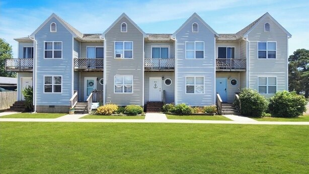 A row of three-story townhouses with a front porch, a small garden, and a clear blue sky. - Central Location~Walk 2 Dining! Beach Pass & Gear! (Chincoteague)