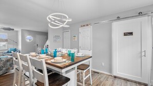 A dining area with a wooden table set for four, white chairs, and a modern pendant light. - Central Location~Walk 2 Dining! Beach Pass & Gear! (Chincoteague)