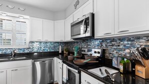 A modern kitchen with white cabinets, a stainless steel dishwasher, a microwave, and a tiled backsplash. - Central Location~Walk 2 Dining! Beach Pass & Gear! (Chincoteague)