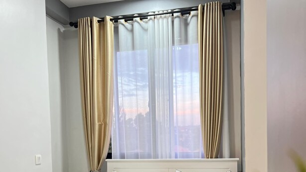 A modern bedroom with a bed, white headboard, and sheer curtains. - Kulambiro Cozy Studio - City Stay (Kampala)