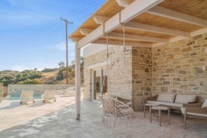 A covered outdoor area with stone walls, a hanging chair, a sofa, and lounge chairs by a pool. - Villa Nala With Pool by Matala (Faistos)
