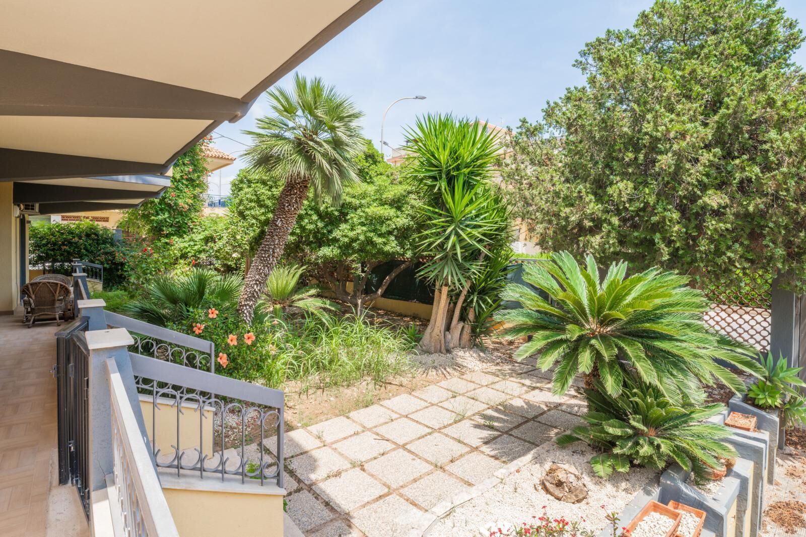 A courtyard with a tiled patio, various plants, and a chair.