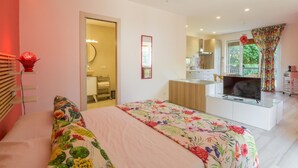 Un dormitorio moderno con cama, una kitchenette pequeña y un baño visible a través de una puerta abierta.