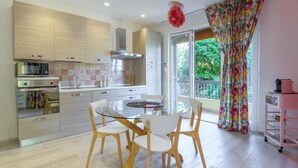 Una cocina moderna con una mesa de comedor de vidrio y sillas, microondas, horno y un ventanal con vistas a zonas verdes.