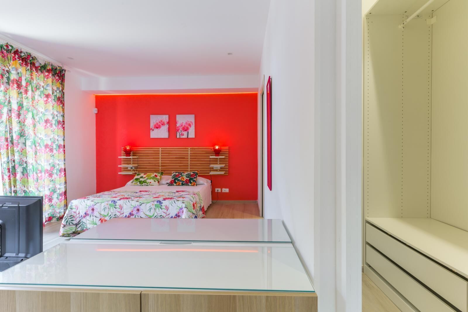 Une chambre à coucher moderne avec un lit, une table en verre et un mur d’accent rouge.