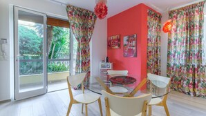 Un comedor con mesa y sillas de vidrio, una pared de acento roja y cortinas con motivos tropicales.