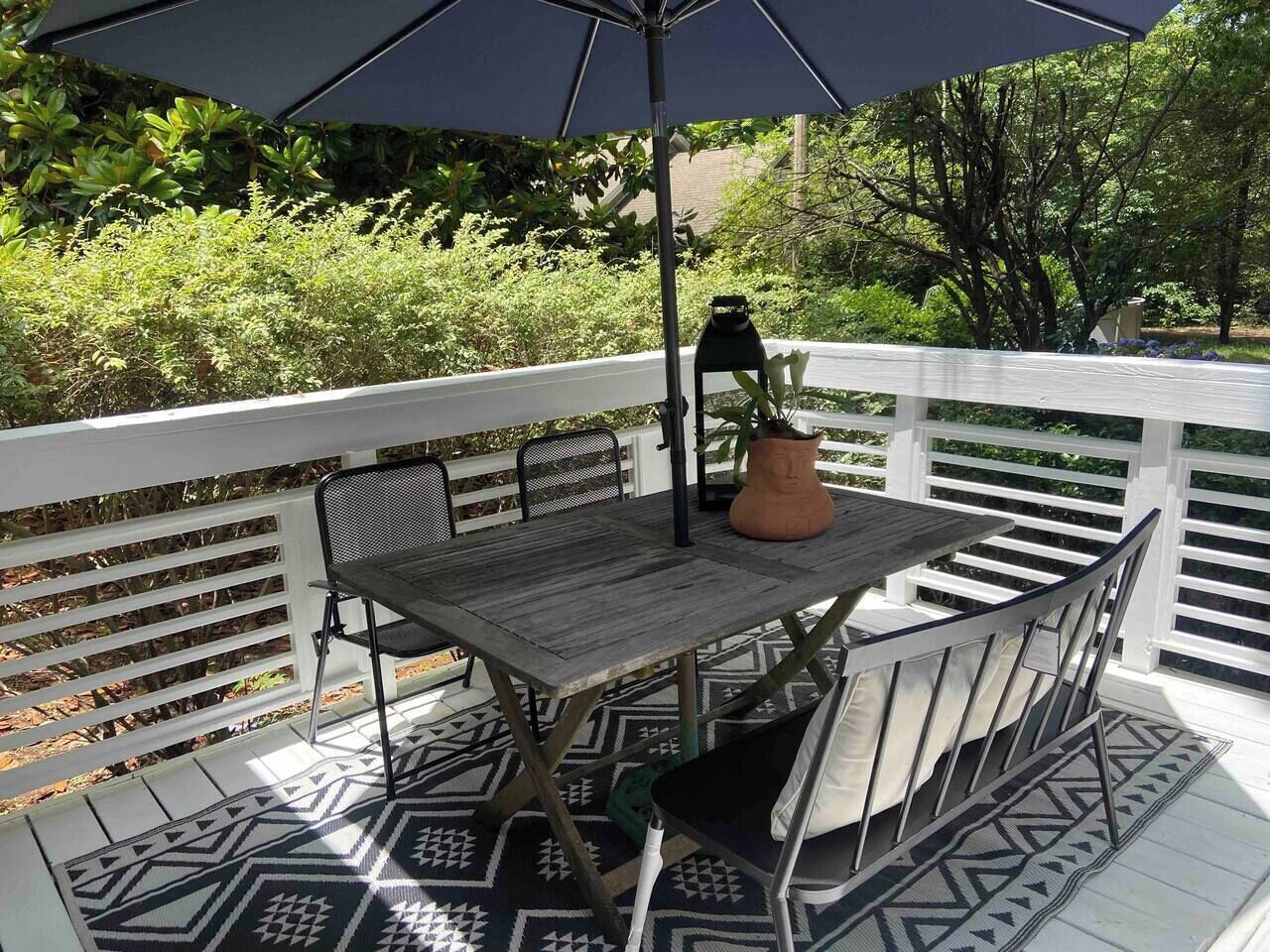 Une terrasse extérieure avec une table et des chaises, une plante en pot et un grand parasol.