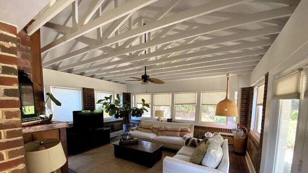 Ein geräumiges Wohnzimmer mit Kamin, Deckenventilator und großen Fenstern, die für natürliches Licht sorgen.