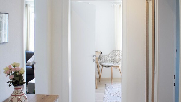 A hallway with a wooden cabinet, a vase with flowers, and a chair in the background.