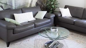 A modern living room with a sectional sofa, a glass coffee table, and a large abstract mural on the wall.