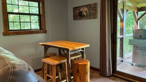 A room with a wooden table and stools, a window with a view of greenery, and a painting on the wall. - Cozy 2-bedroom cabin in beautiful Blairsville with AC, WiFi (Blairsville)