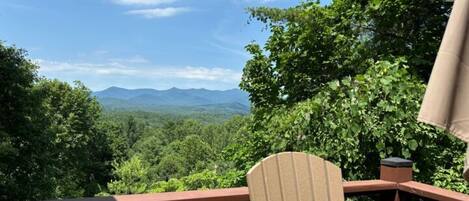 A deck with a chair and table, overlooking a forested landscape with mountains in the distance.