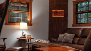 A cozy living room with a leather sofa, a wooden coffee table, a small side table with a lamp, and a framed welcome sign. - Cozy 2-bedroom cabin in beautiful Blairsville with AC, WiFi (Blairsville)