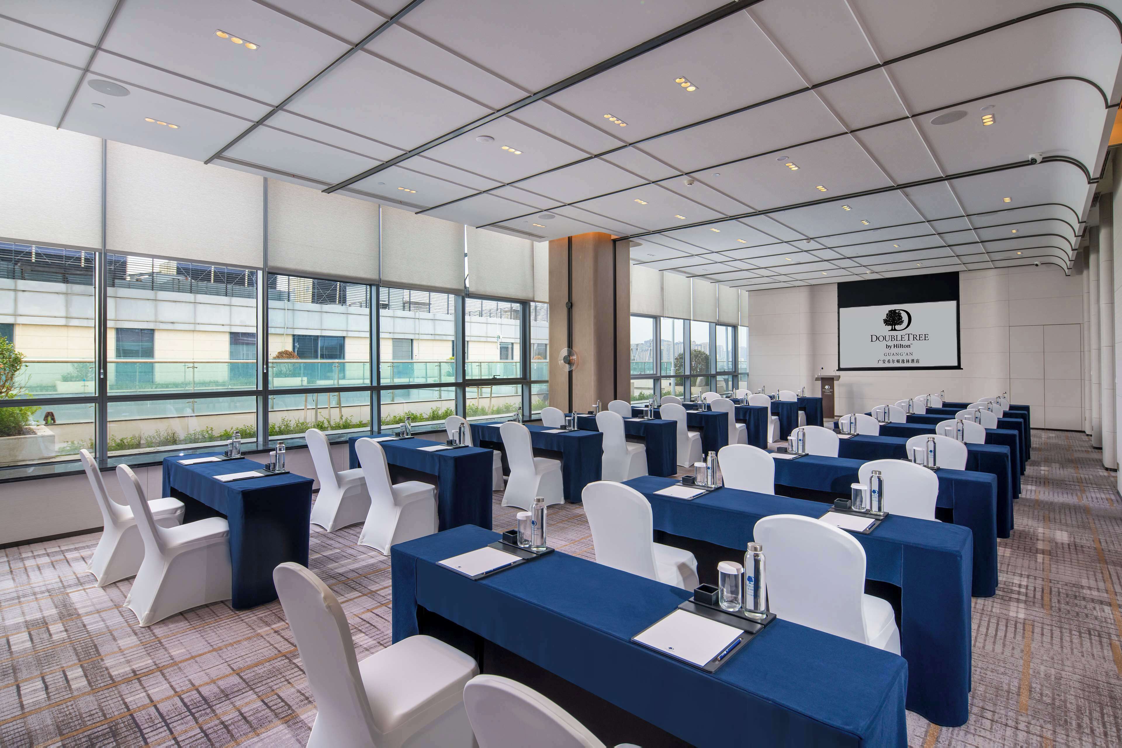 Un salón de conferencias con mesas, sillas y una pantalla grande que muestra el logo de DoubleTree.