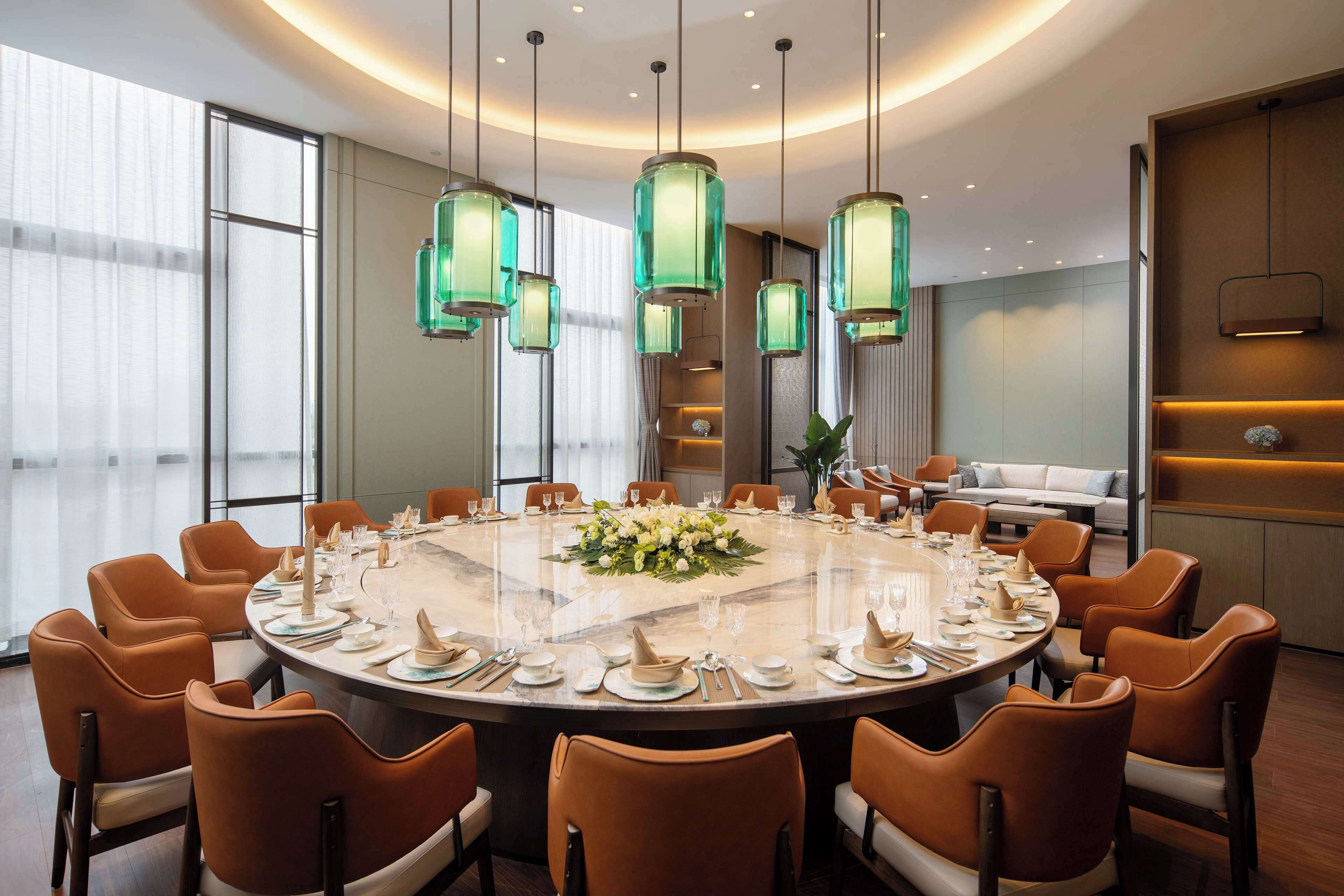 A modern conference room with a round table, orange chairs, and green pendant lights.