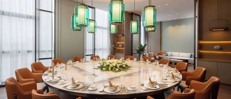A modern conference room with a round table, orange chairs, and green pendant lights.