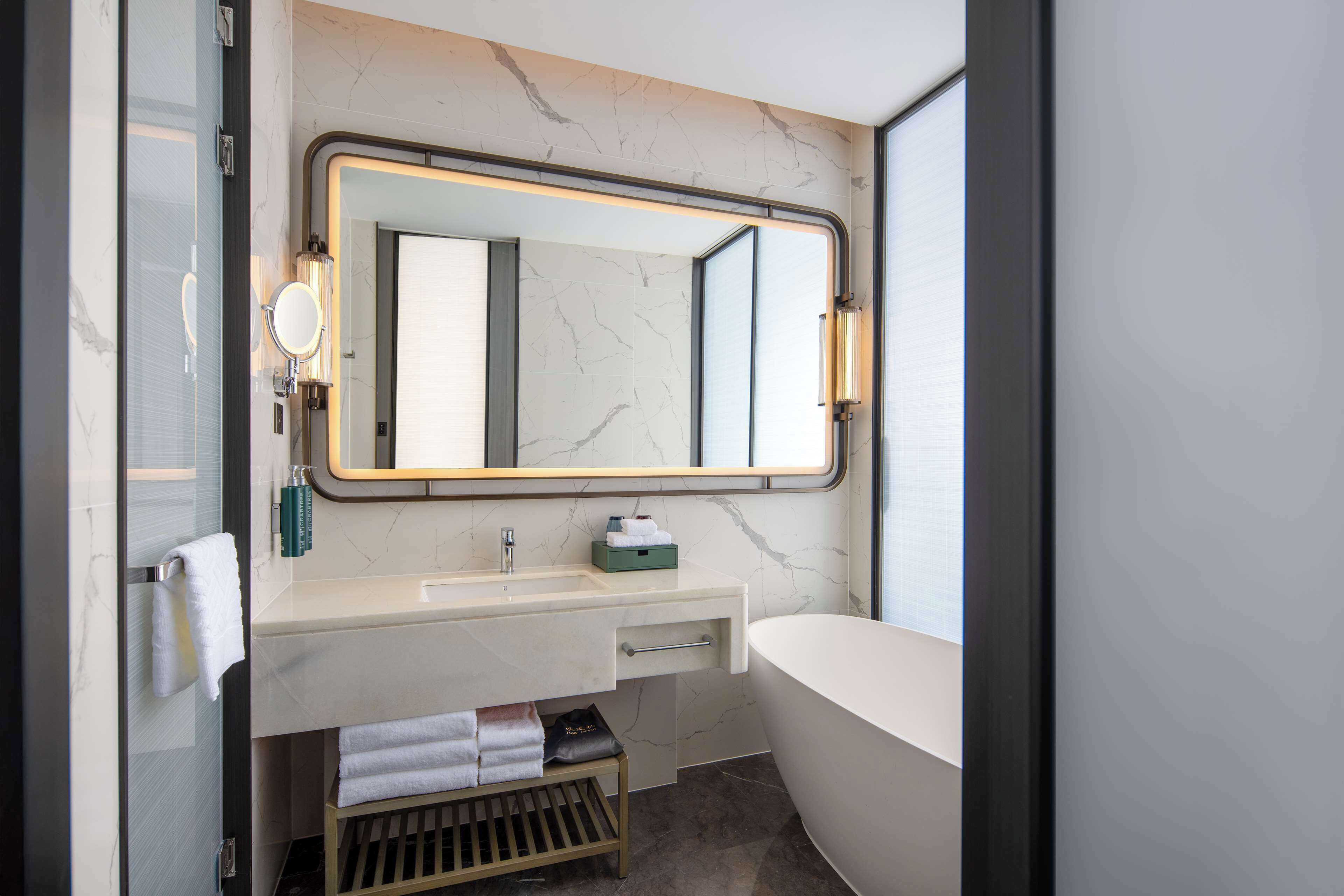 A modern bathroom with a large mirror, a bathtub, a vanity with a sink, and a towel rack.