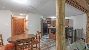 A dining area with a wooden table and chairs, a kitchen with a refrigerator and microwave, and a living area with a sofa and a wooden post. - Champagne Powder Chalet! Best Ski In/Out at Big White. Sleeps up to 7ppl. (Beaverdell)