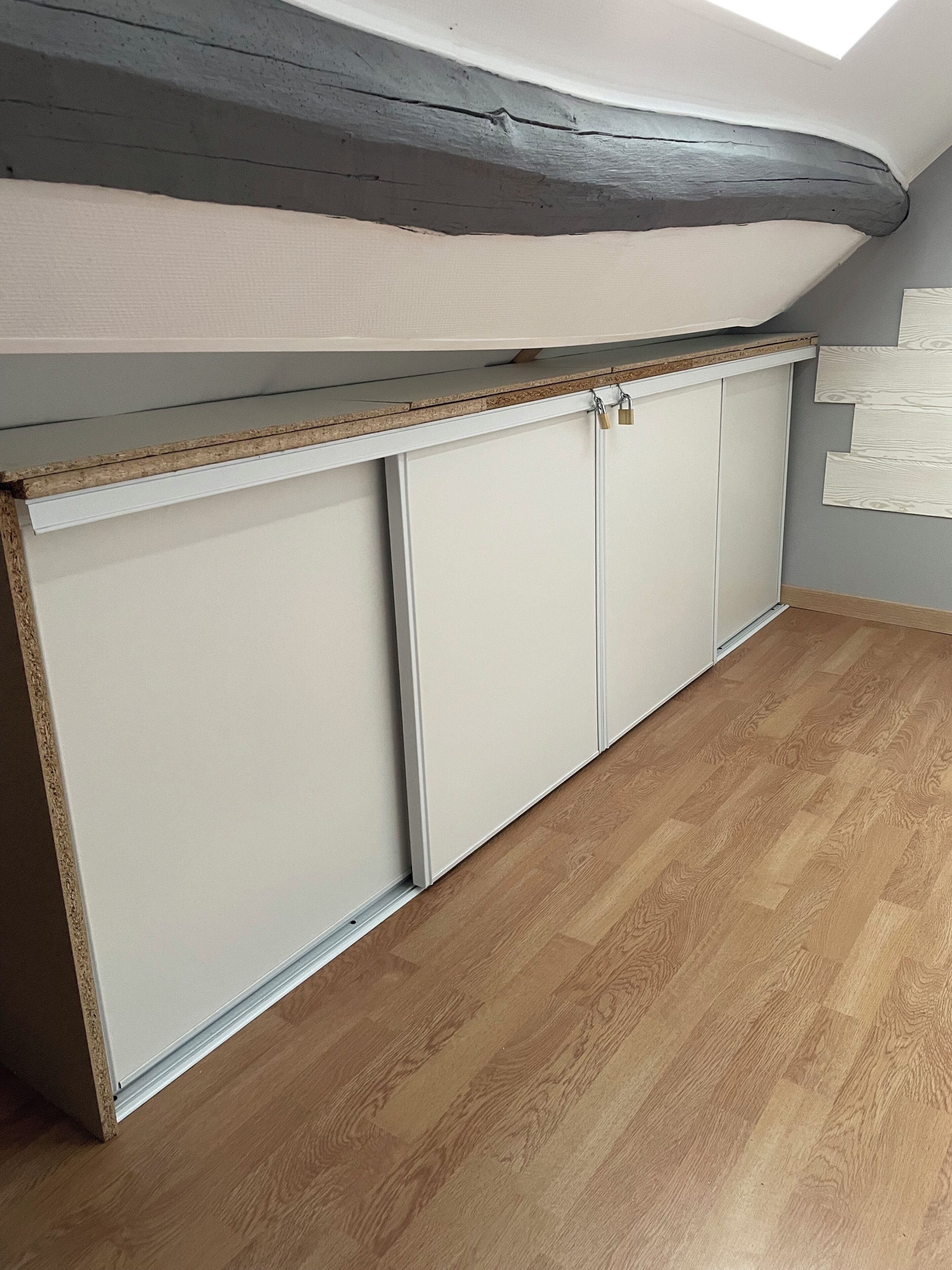 Una habitación con techo inclinado, suelo de madera y un armario empotrado blanco con dos puertas.