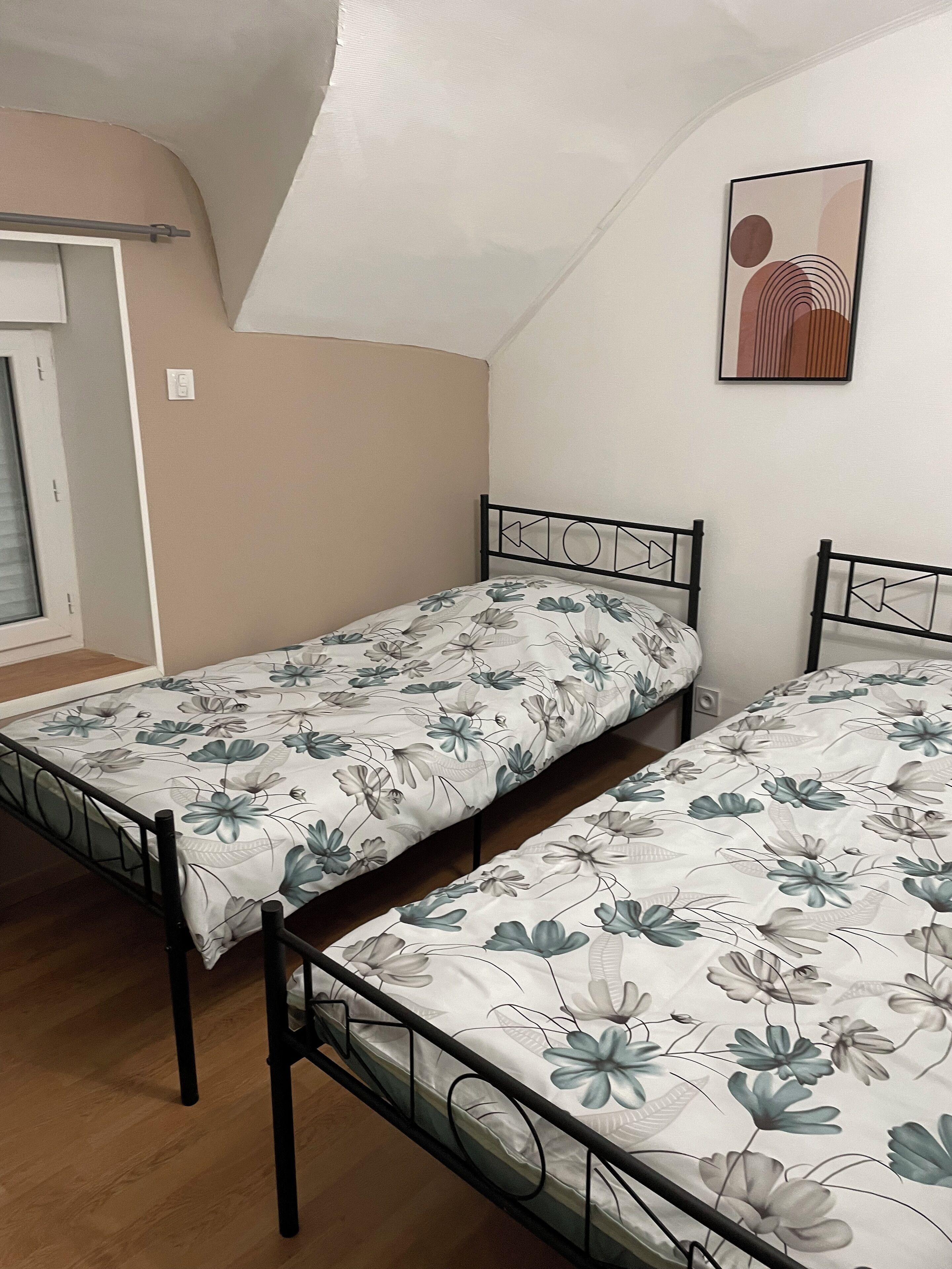 A bedroom with two single beds, a window, and a wall-mounted picture.