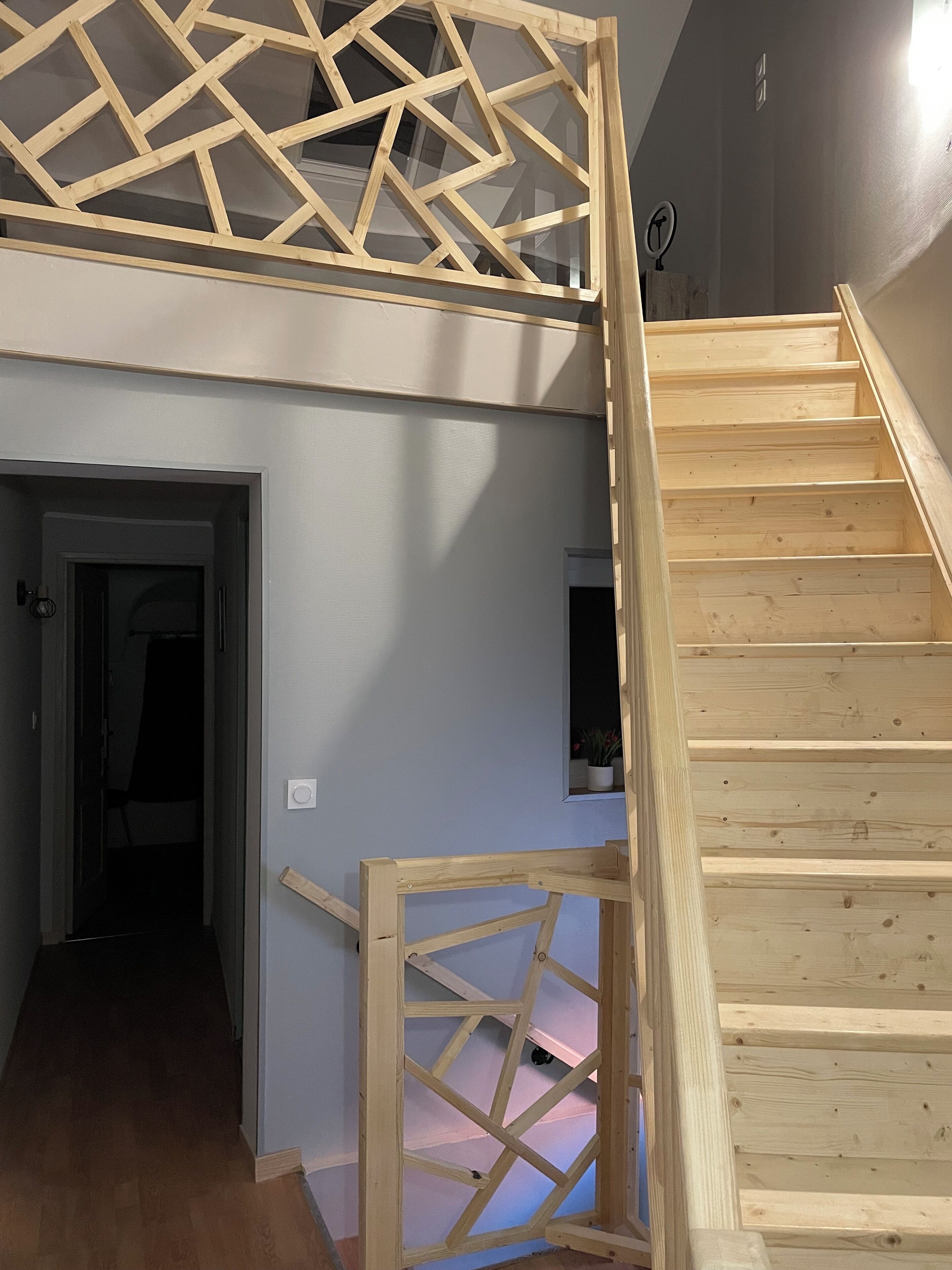 A wooden staircase with a geometric railing design, leading to a second-floor landing.