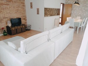 A modern living room with a white sofa, a television, and a dining area with white chairs and a table. - [300 meters from the ocean - Free parking] Wi-Fi | Air conditioning (Camaiore)